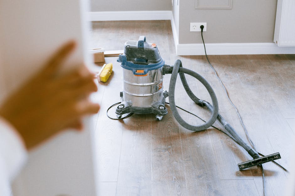 A person wearing orange cleaning gloves is adjusting a illuminated sign with black letters spelling 'CLEANING HOME' on a white background. The sign is placed on a table or countertop in a well-lit roo